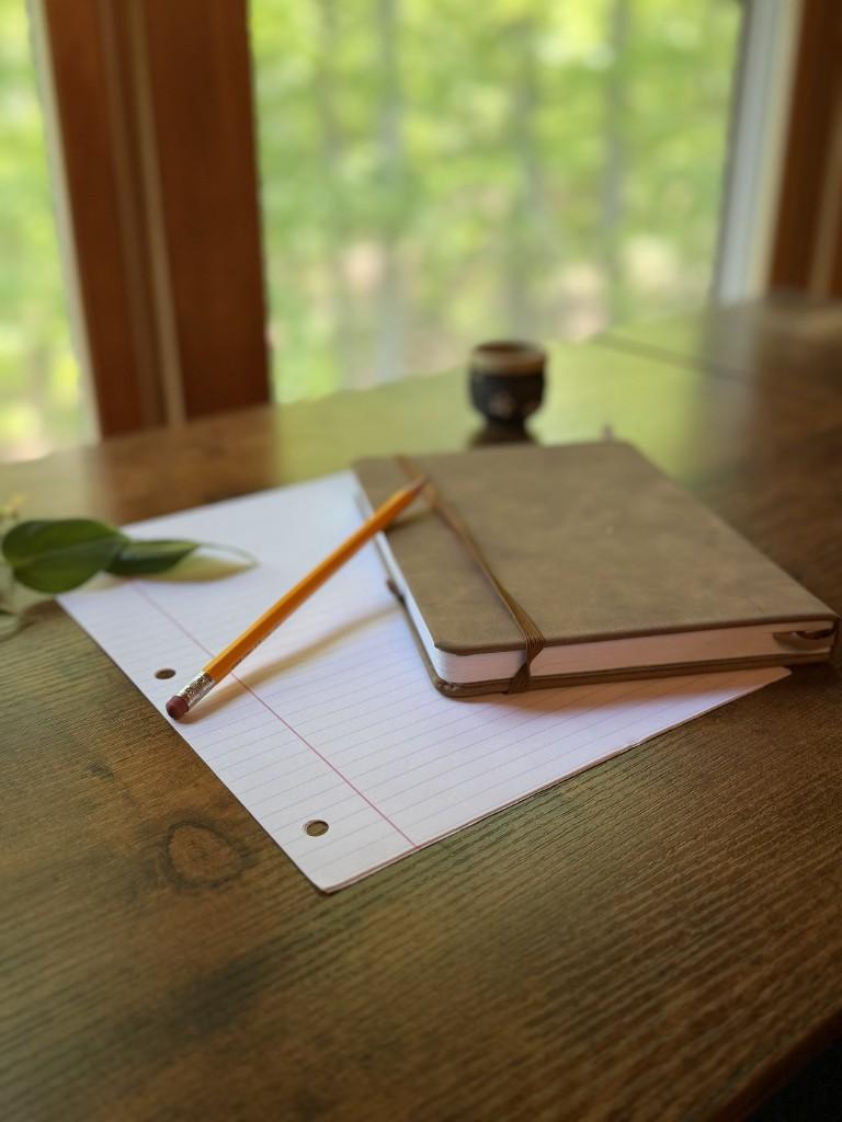 Notebook and pencil on a wooden desk by a window, suggesting a calm creative workspace at Inspire Barn